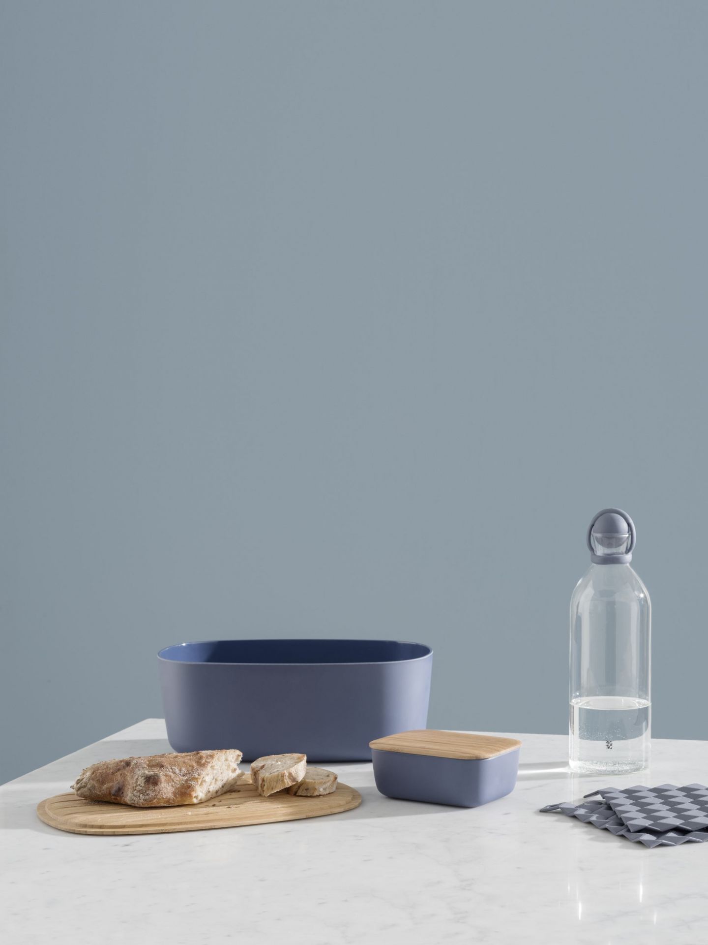 Dunkelblaue BOX-IT Butterdose von RIG TIG by Stelton mit Holzdeckel neben Brot und Wasserflasche.