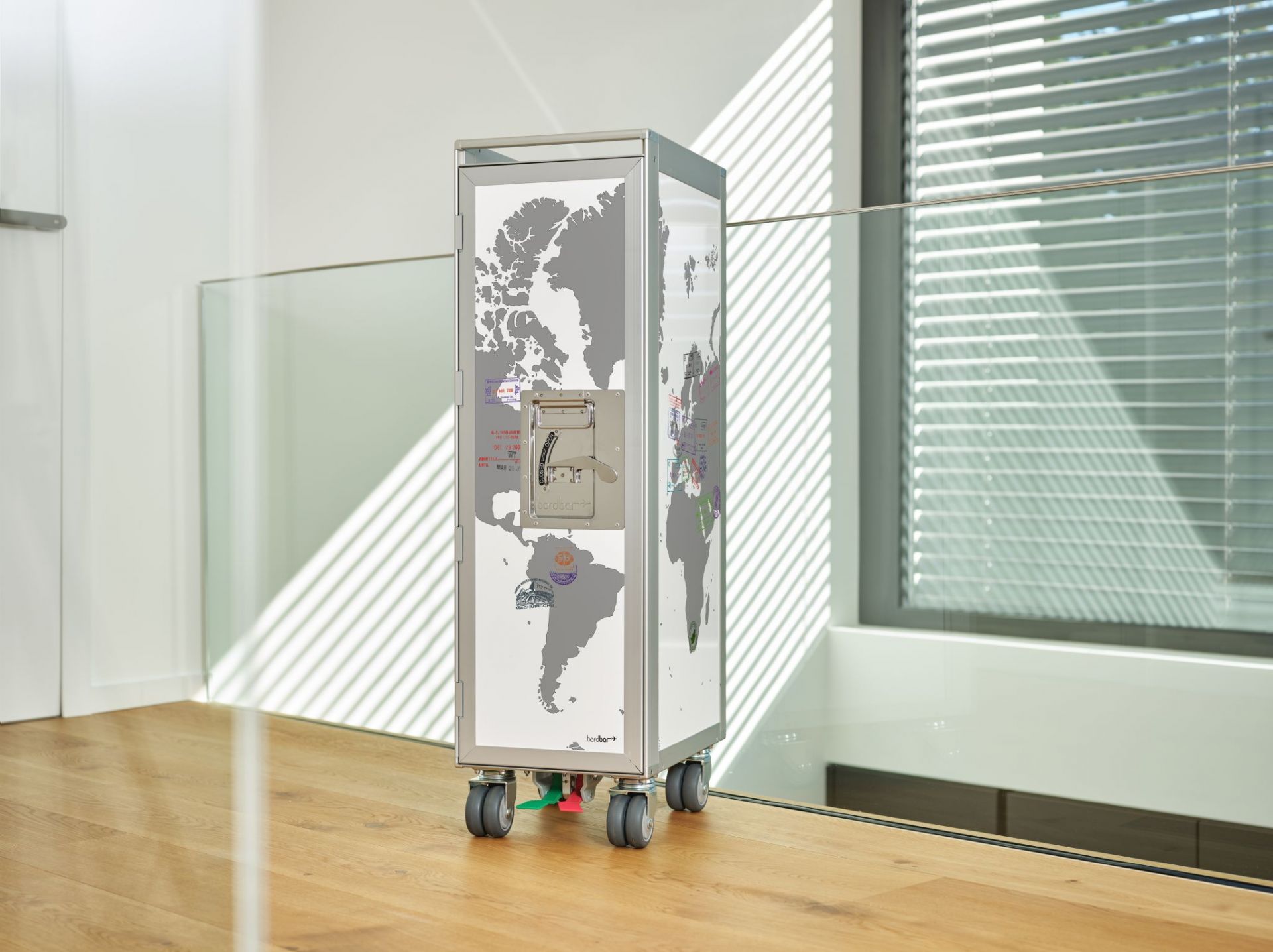 Grauer Passport Flugzeugtrolley Bordbar mit Weltkarte und Stempeln auf hellem Holzboden. Praktische Bordbar für Zuhause.