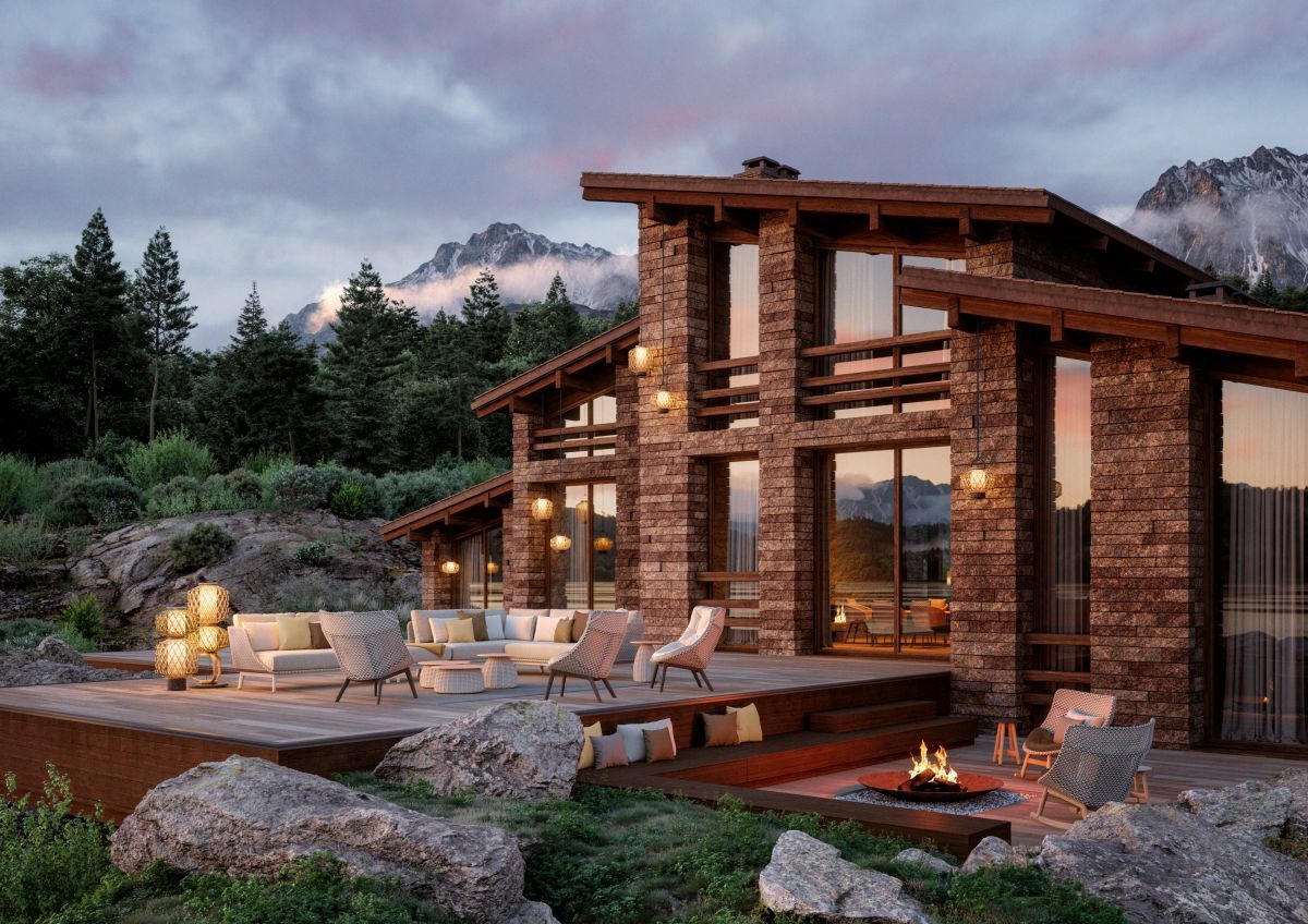 Mbrace Hocker von Dedon mit Polster auf Holzterrasse vor einem luxuriösen Steinhaus.