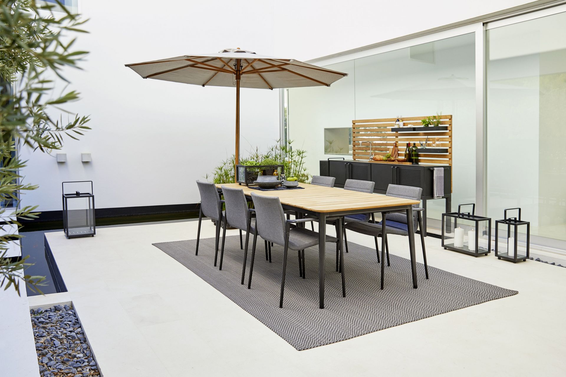 Essbereich im Freien mit Cane-Line Core Outdoor Stühlen AirTouch, Tisch und Sonnenschirm.