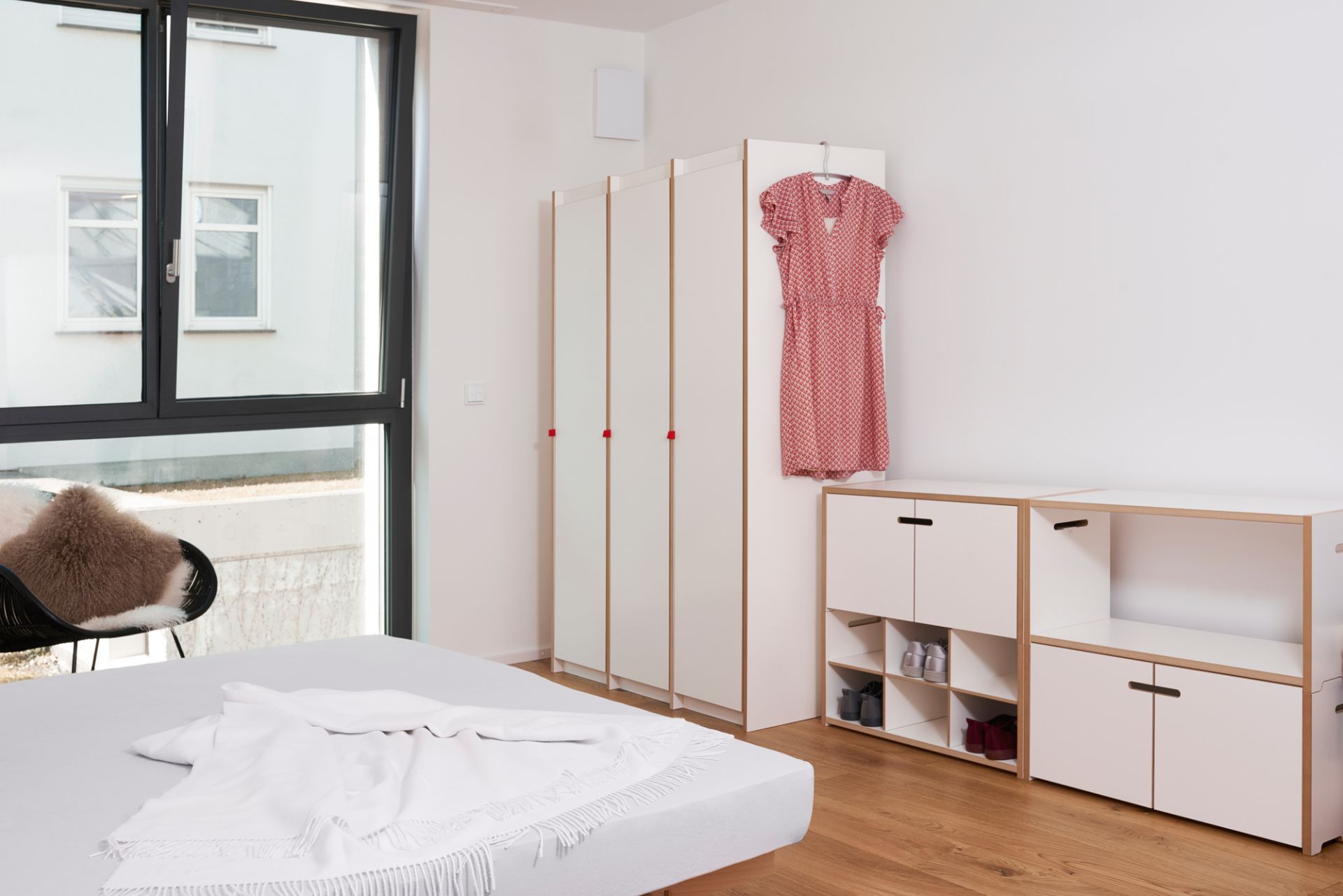 Helles Schlafzimmer mit Tojo Steh Schrank Grundmodul, Kleiderschrank und Regalen in minimalistischem Design.