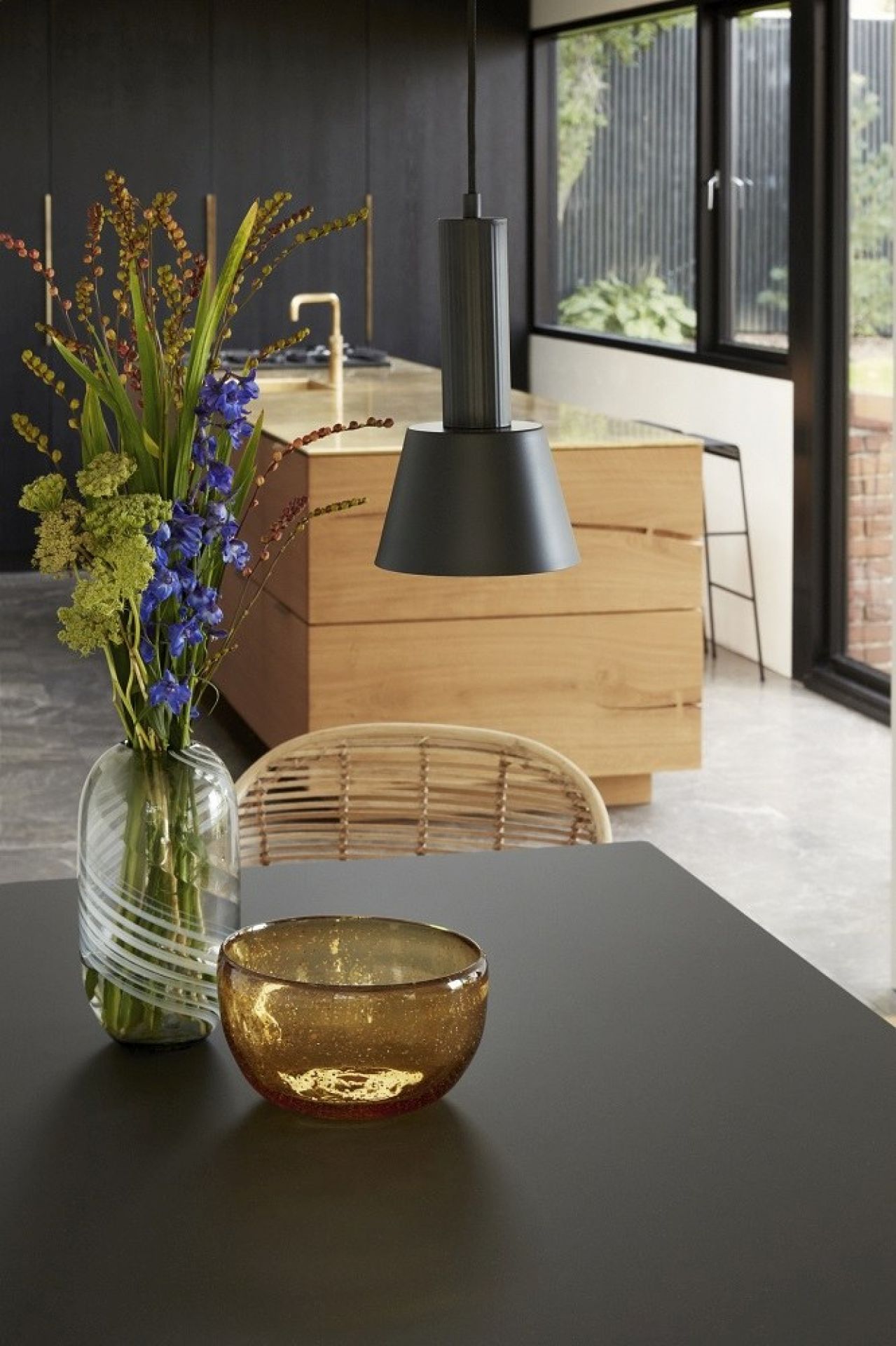 Nahaufnahme einer grünen Glasvase mit weißen Wirbeln und Blumen auf einem Esstisch.