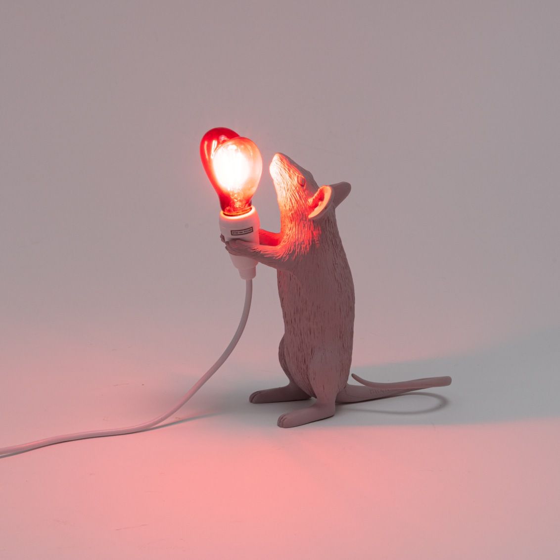 Seletti Mouse Lamp Step Love Edition: Graue Maus hält leuchtende Glühbirne als Tischleuchte.