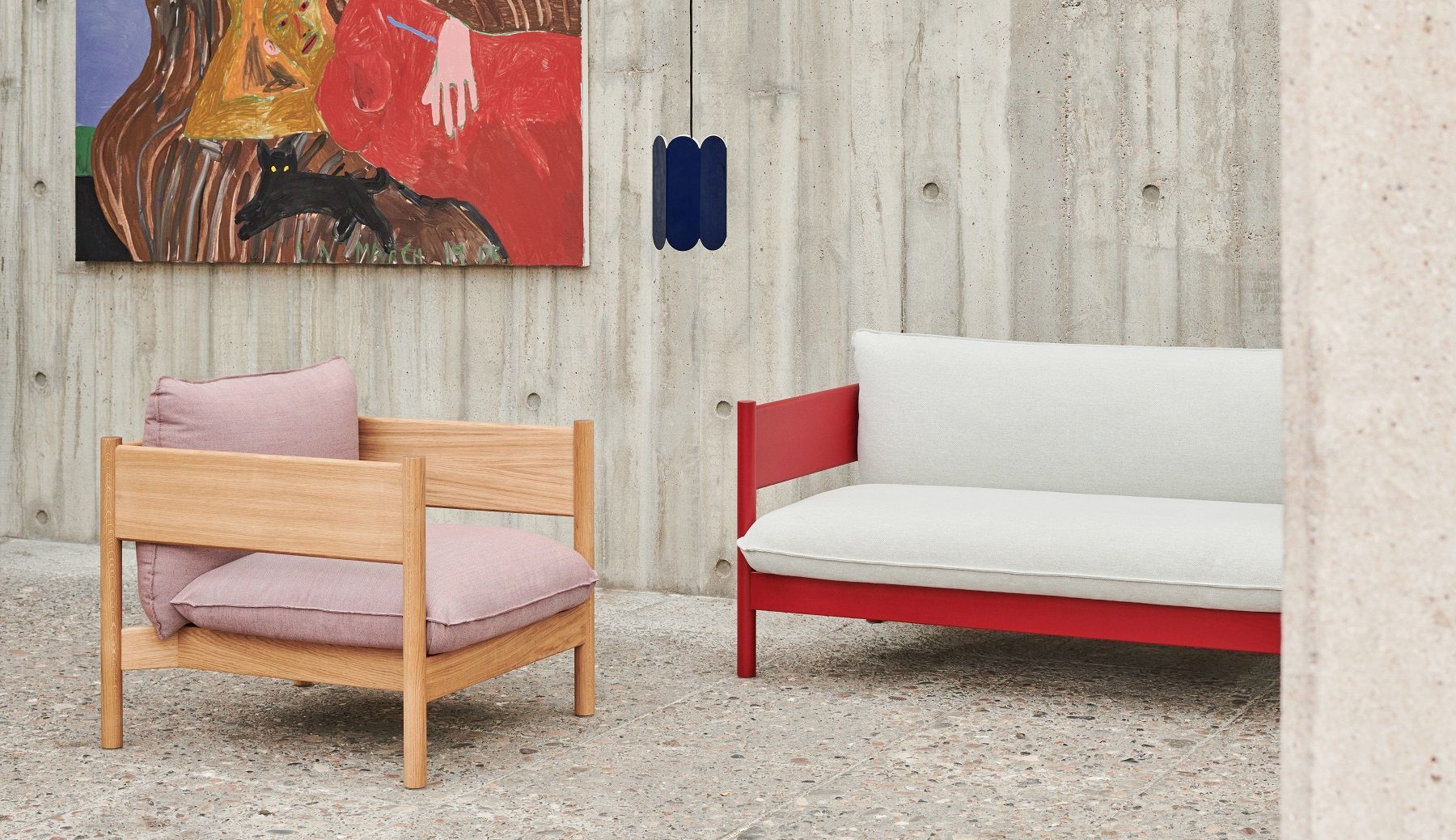 Arbour Sofa von Hay: Sessel mit rosa Kissen und rotes Sofa vor Betonwand.