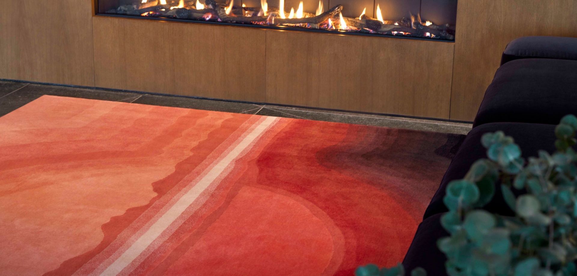 Sunset Rug Teppich mit Farbverlauf in Rot- und Orangetönen vor einem Kamin.