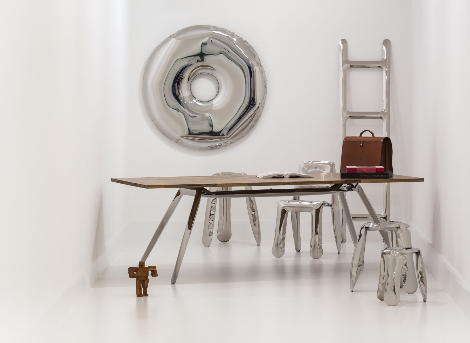 Silberner Rondo Spiegel von Zieta Design an weißer Wand über Holztisch mit Stühlen.