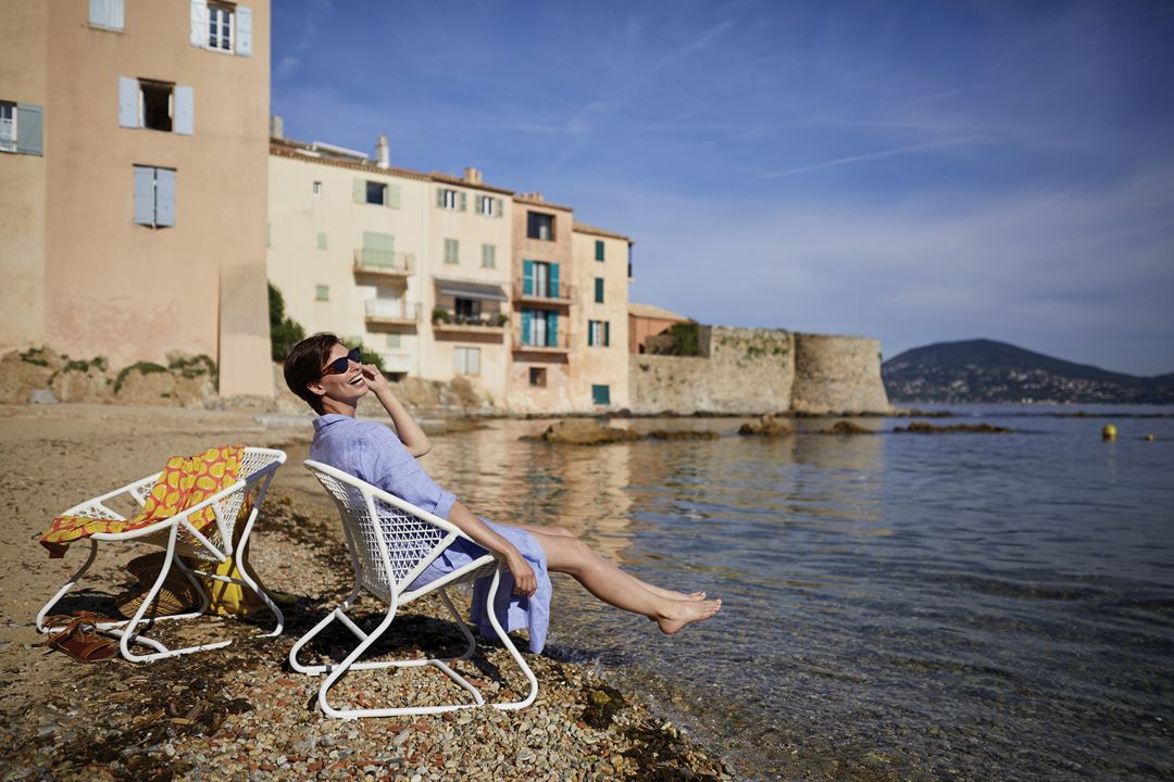Frau entspannt im weißen Fermob Sixties Outdoor Sessel am Strand mit Meerblick.