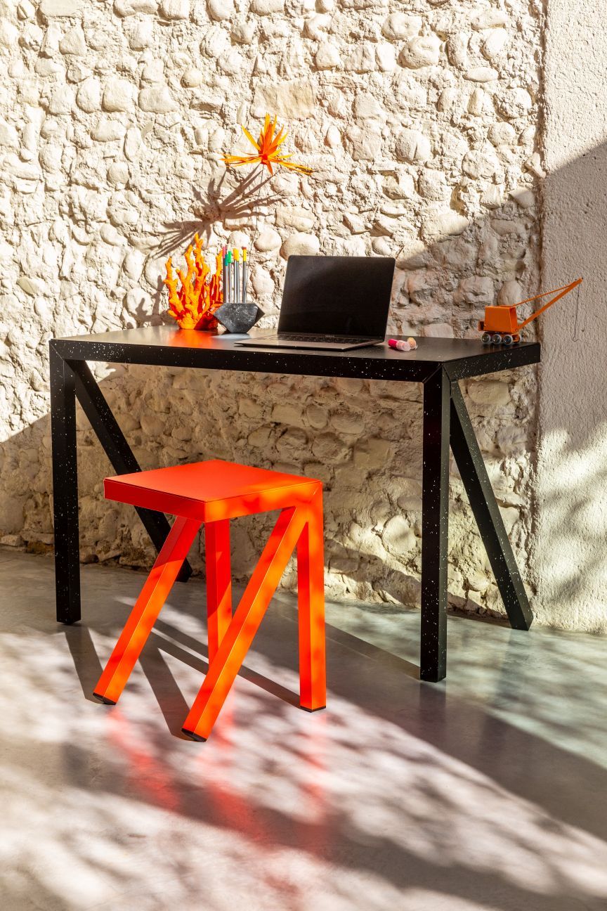 Bureaurama Hocker von Magis, orangefarbener Barhocker vor Schreibtisch und Steinwand. Design Büromöbel.