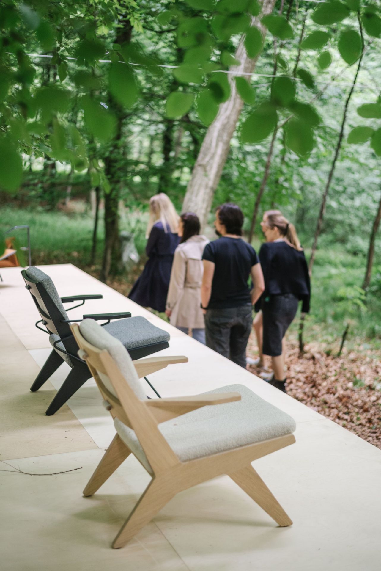 Nahaufnahme von zwei Toggle Sesseln aus Holz von Prostoria, minimalistisches Design, im Hintergrund Personen und Bäume.