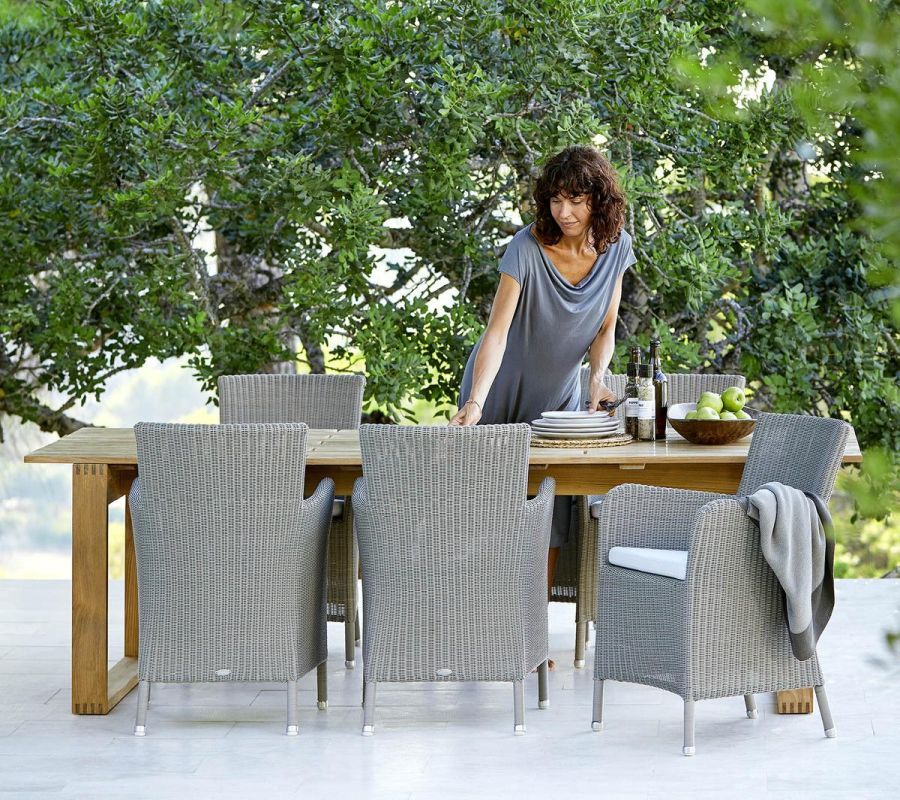Endless Esstisch von Cane-Line mit Flechtstühlen im Garten, gedeckt für ein Essen im Freien.