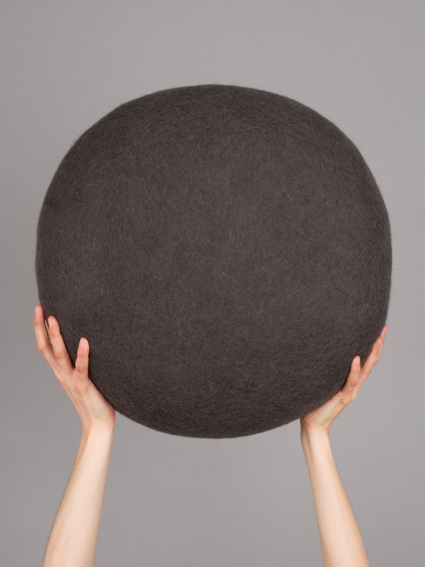 Hände halten einen grauen Filz Pouf Hocker von myfelt, Modell Kuno.