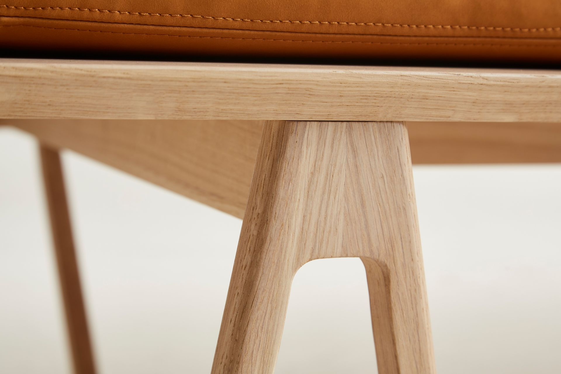 Detailaufnahme der Eichenholzbeine der Level Daybed Liege von Woud mit cognacfarbenem Lederpolster.