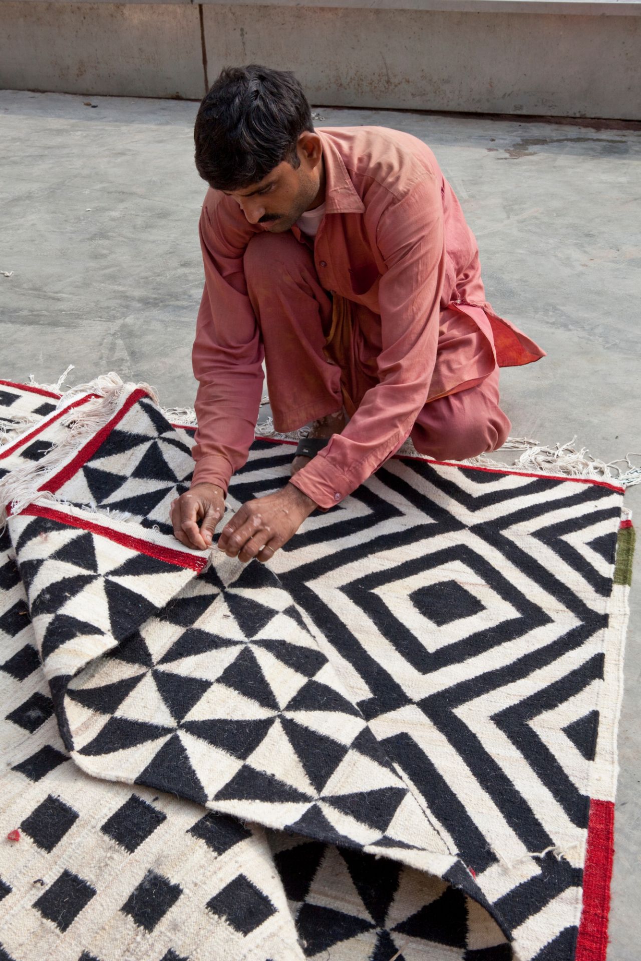 Mann inspiziert Nanimarquina Teppich mit geometrischem Muster, handgefertigter Wollteppich für Wohnzimmer.