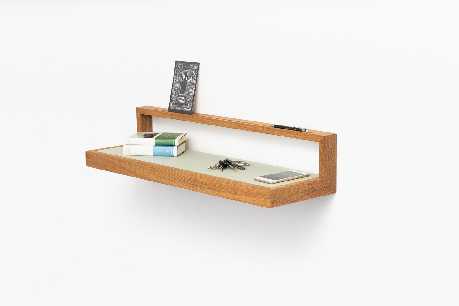 Pistazienfarbenes Wandboard "buck3" aus Holz mit Büchern, Schlüssel und Smartphone als Dekoration.