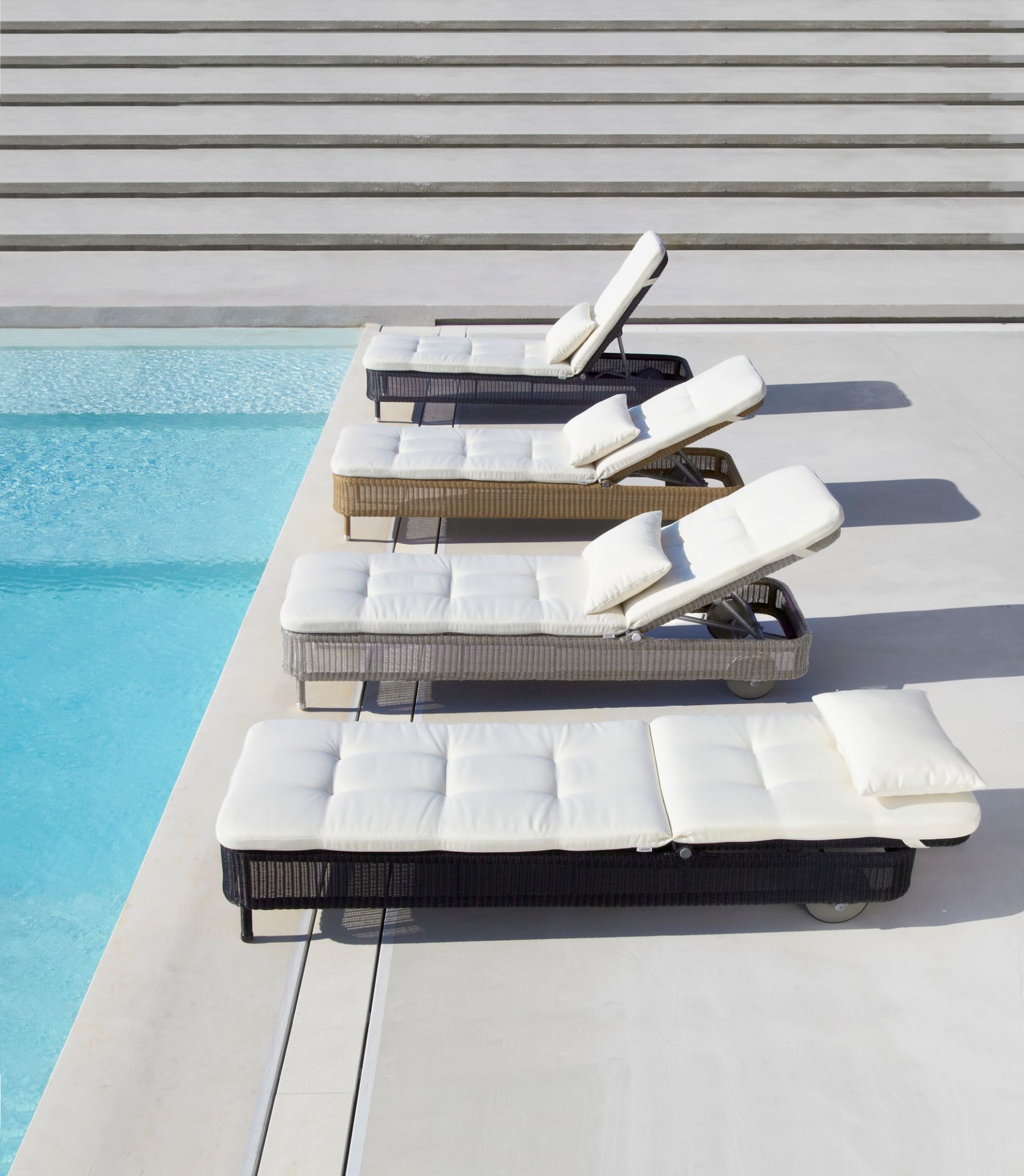 Mehrere Cane-Line Sonnenliegen am Pool, darunter die Presley Outdoor Sonnenliege in Taupe.