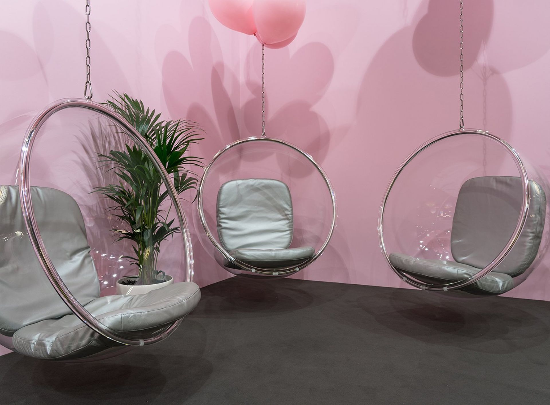 Drei transparente Bubble Hängesessel mit grauen Kissen vor rosa Wand. Design Hängesessel für modernes Wohnen.
