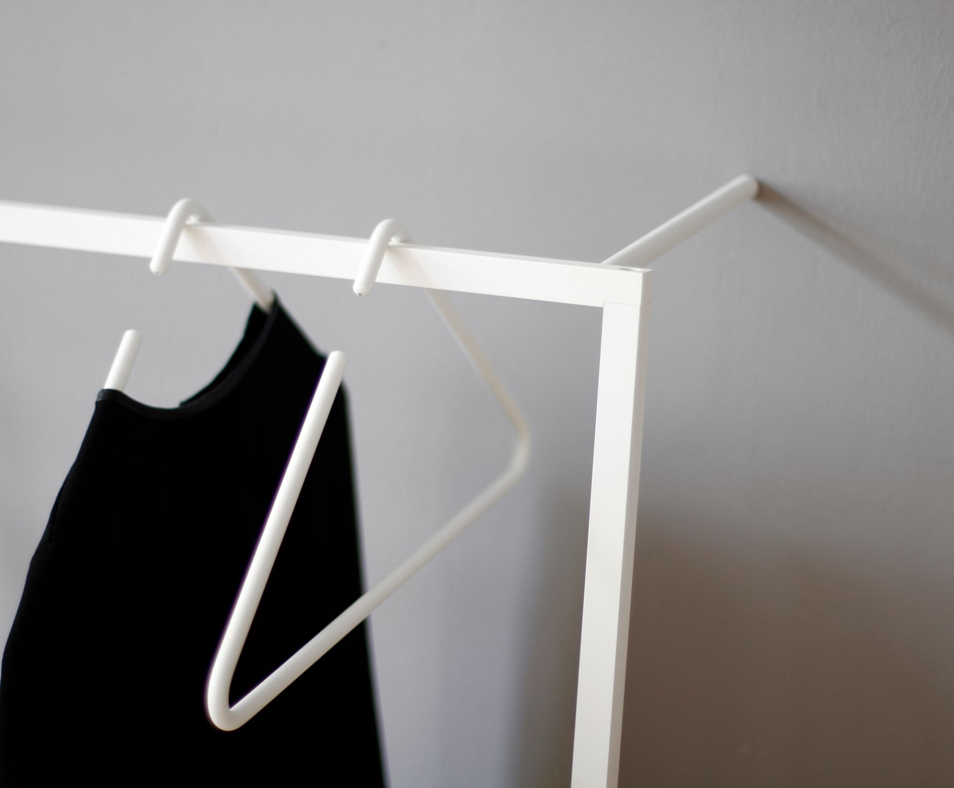 Detailaufnahme: Weißer Triangle Kleiderbügel von Roomsafari mit schwarzem Kleid an einer minimalistischen Garderobe.