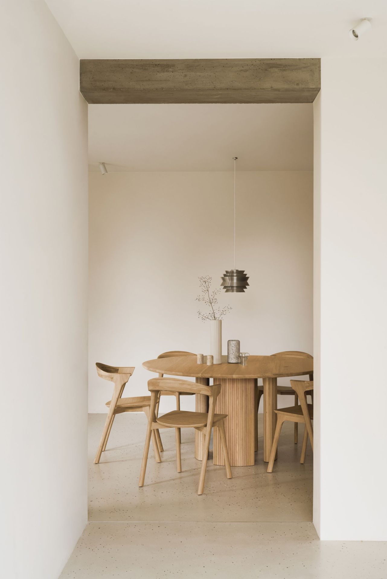 Ethnicraft Roller Max Tisch: Runder Holztisch mit geriffeltem Sockel und passenden Holzstühlen in minimalistischem Interieur.