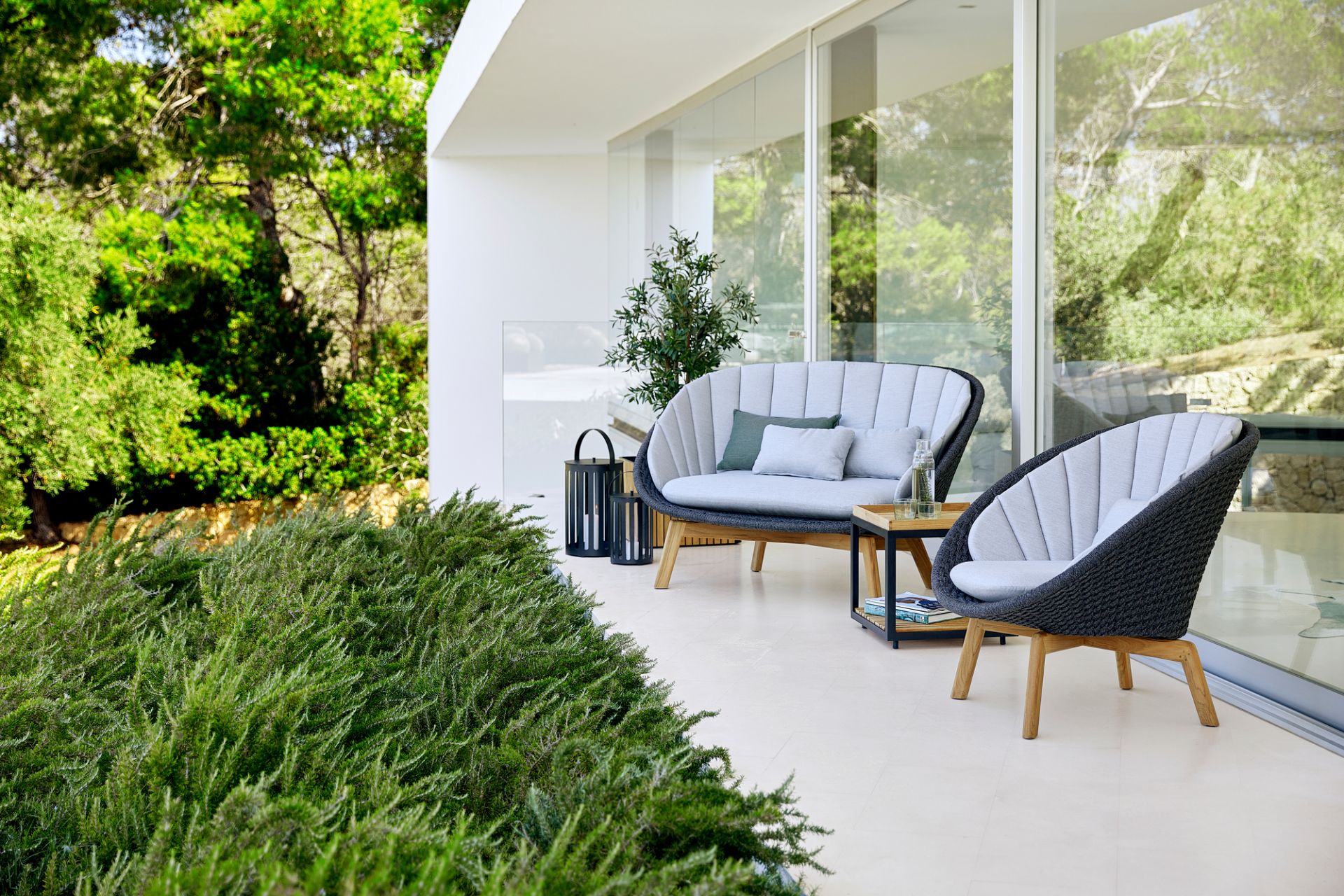 Peacock Outdoor Lounge Set von Cane-Line: 2-Sitzer Sofa und Sessel auf einer Terrasse.