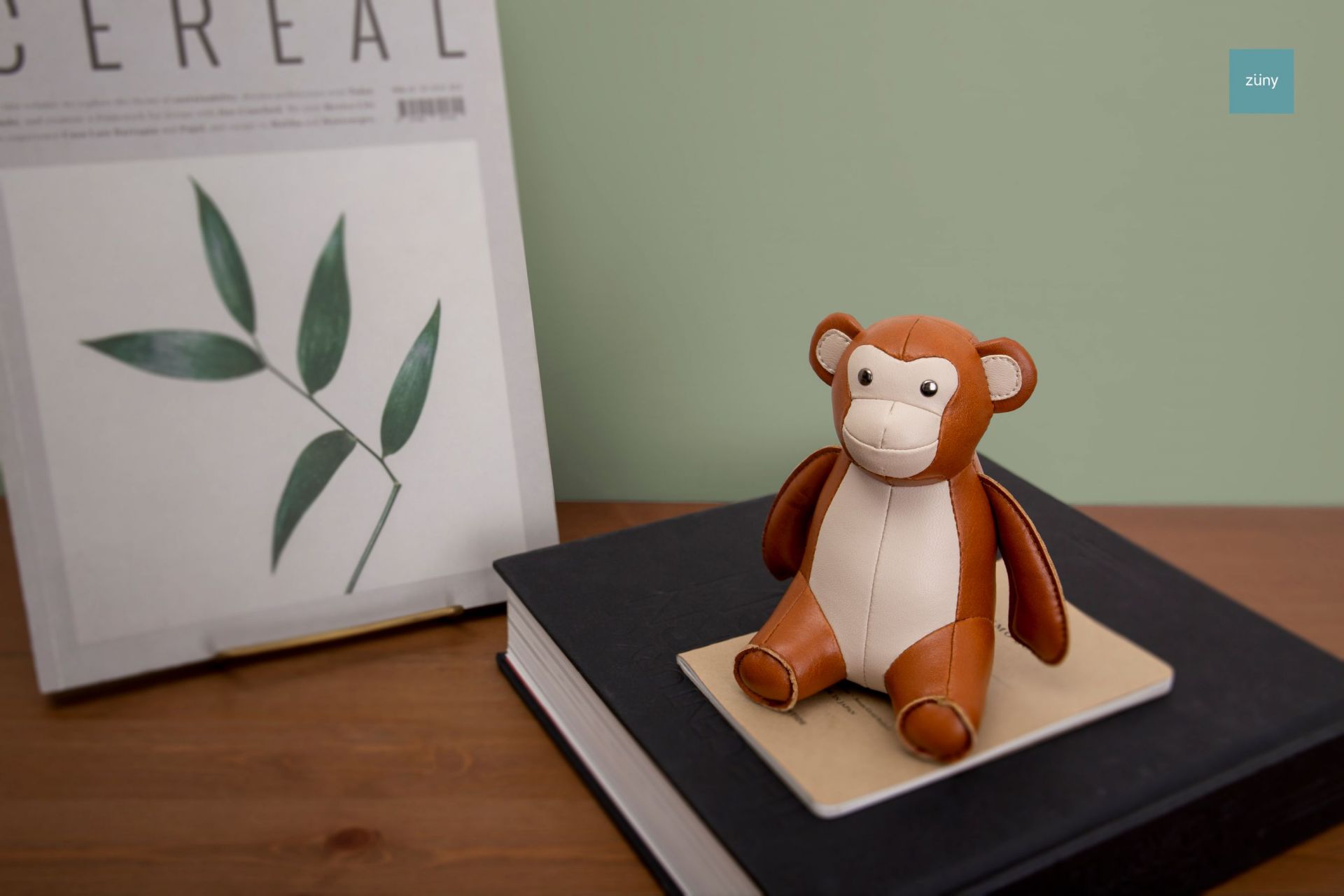 Briefbeschwerer Affe Tan/Weizen Züny aus Kunstleder sitzt auf einem Buch. Dekoration und Accessoire.