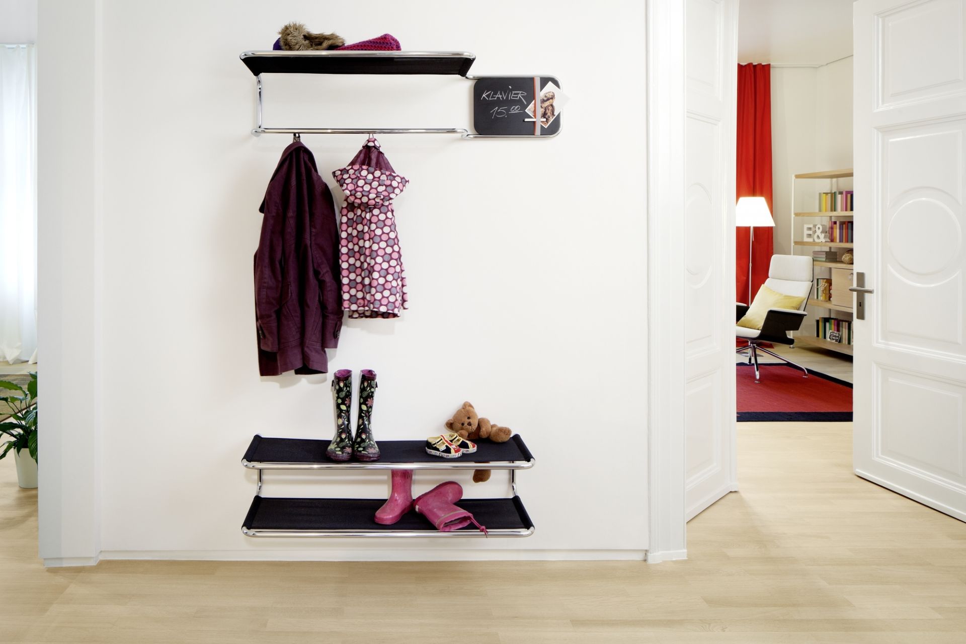 Thonet Wandgarderobe S 1520 mit Kleidung, Stiefeln und Accessoires an einer weißen Wand im Flur.