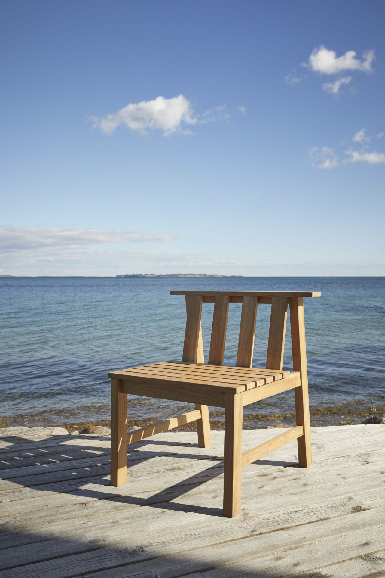 Cadence Stuhl aus Teakholz von Skagerak, ein Outdoor Stuhl vor blauem Meer.