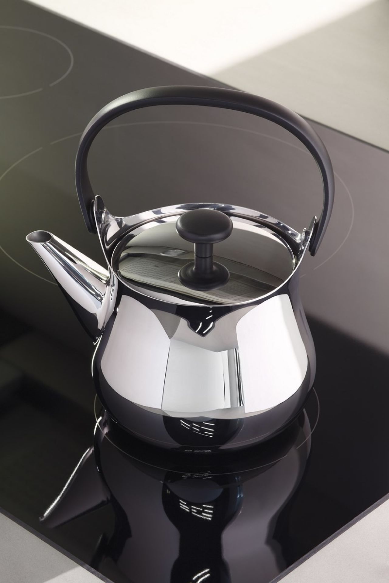 Nahaufnahme der glänzenden Alessi Cha Teekanne NF01 auf einem schwarzen Induktionskochfeld.