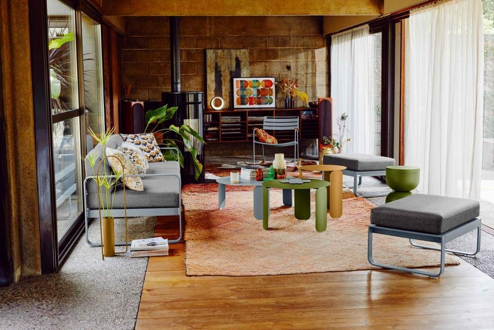 Wohnzimmer mit Fermob Hoopik Tischleuchte, Couch, Teppich und Hockern in verschiedenen Farben.