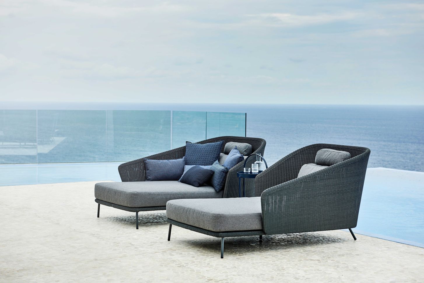 Zwei graue Cane-Line Outdoor Daybeds mit blauen Kissen und Meerblick. Luxuriöse Gartenmöbel.