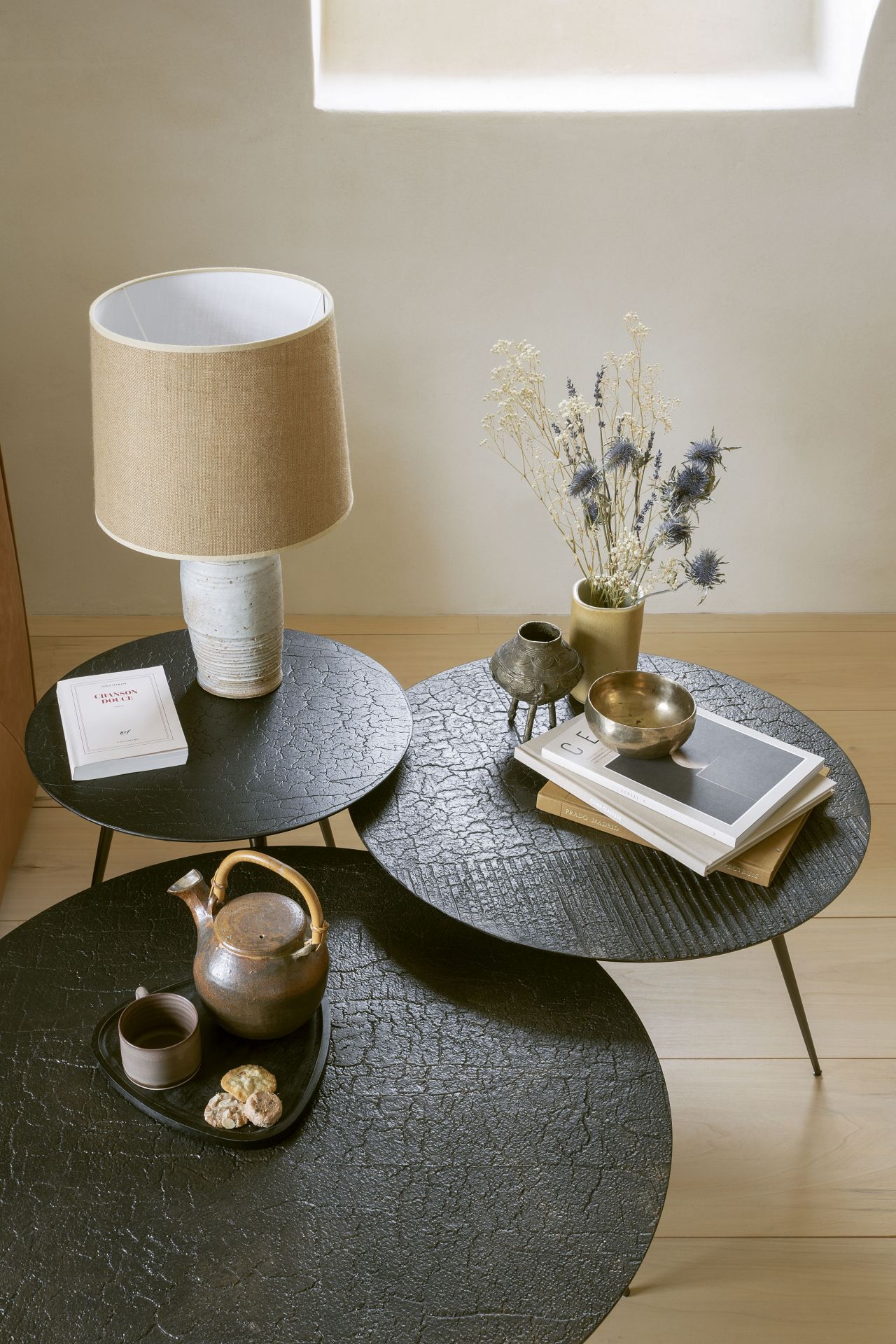 Ethnicraft Luna Couchtisch ∅50 cm: Drei runde, schwarze Tische mit Deko, Teekanne und Lampe.