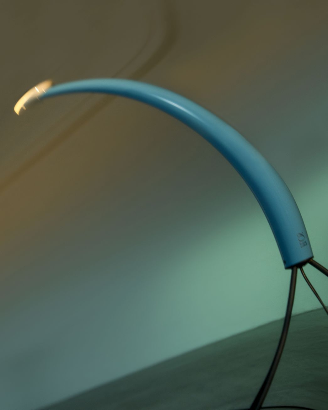 Blaue Bogenleuchte, ähnlich der Flos Luminator, mit schwarzem Fuß und warmem Lichtschein.