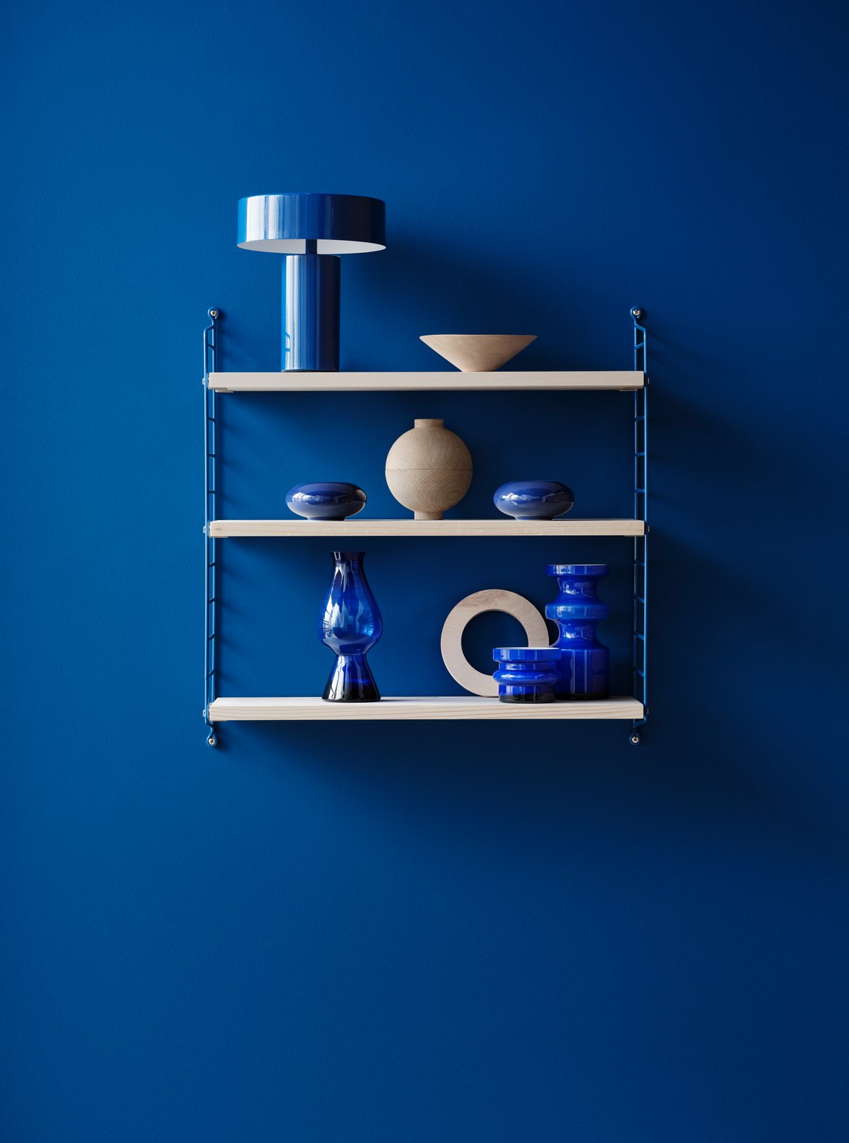 String Pocket Regal in Blau mit Deko-Elementen vor blauer Wand. Modernes String Furniture Design.