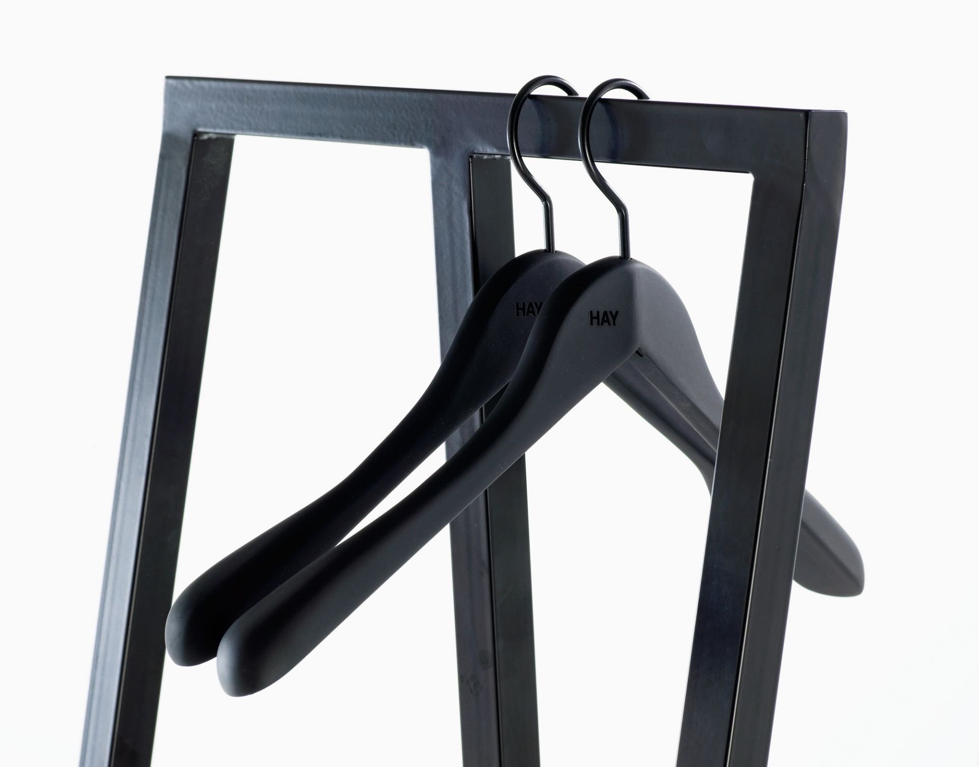 Schwarze Hay Kleiderbügel (Soft Coat Hanger Wide) auf einer Garderobenstange, Detailaufnahme für E-Commerce.