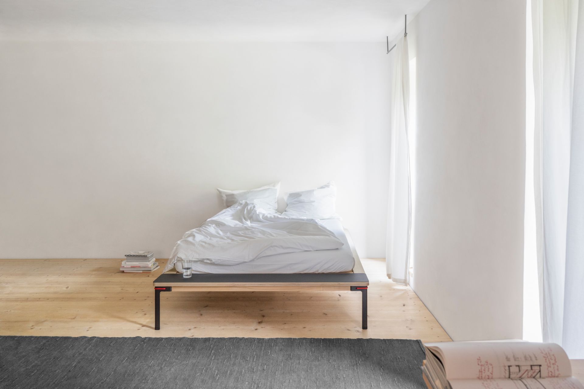 Minimalistisches Seiltänzer Bett von Nils Holger Moormann, rot akzentuiert, 160x200 cm, mit weißer Bettwäsche.