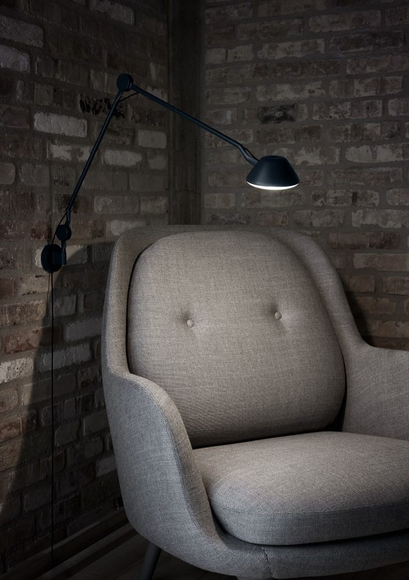 AQ01 Wandleuchte von Fritz Hansen, weiße Design Lampe über einem Sessel an Backsteinwand.