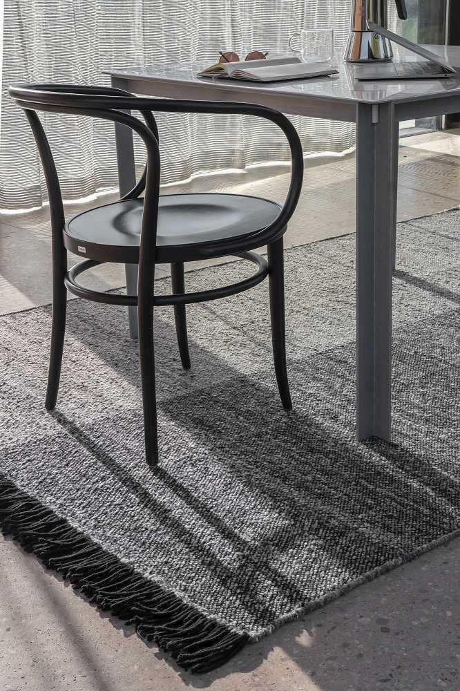 Detailaufnahme: Grauer Nanimarquina Teppich mit Fransen, Teil der Re-Rug Collection, unter Tisch und Stuhl.