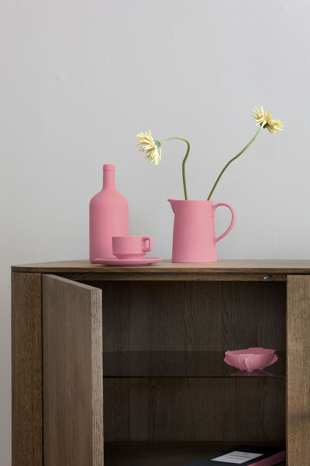 Loud Sideboard aus hellem Eichenholz mit offener Tür und pinkfarbener Dekoration.