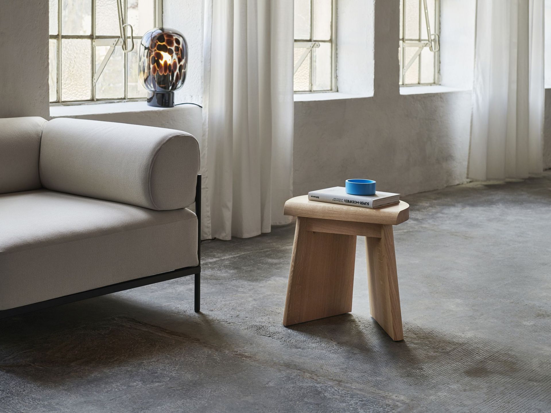 Flakes Tischleuchte Favius in Rauchgrau und Schwarz auf Fensterbank neben Sofa im Wohnzimmer.