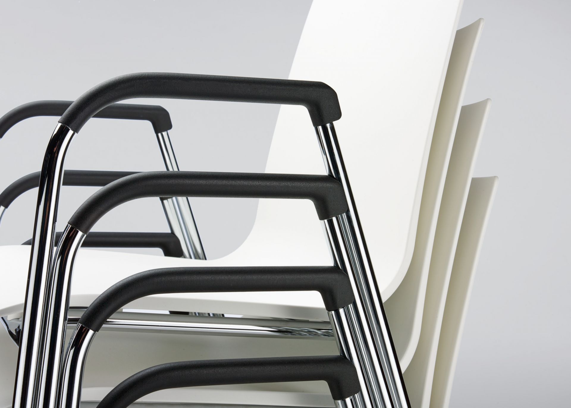 Detailaufnahme von gestapelten S 260 F Stühlen mit Armlehne von Thonet, weißer Sitzschale und Chromgestell.