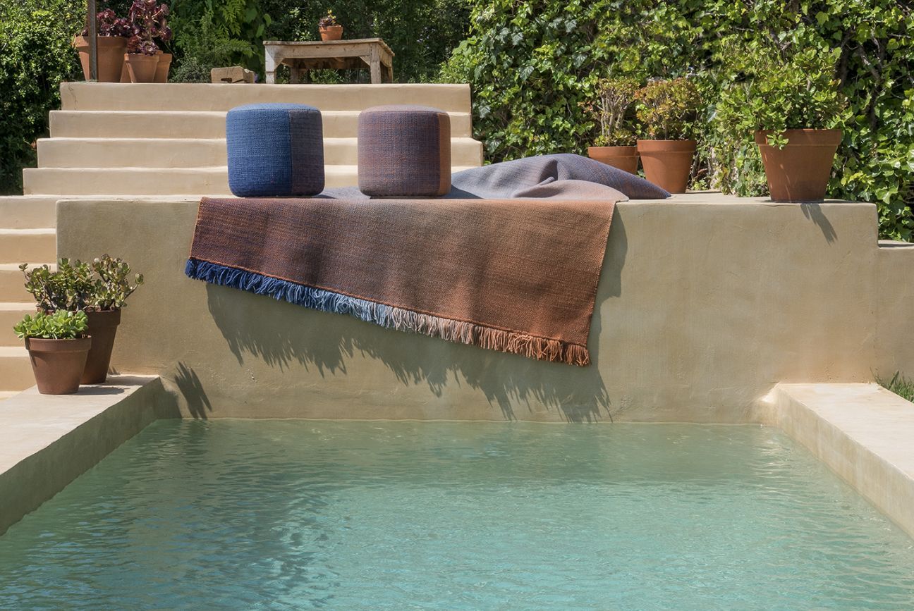 Zwei Nanimarquina Shade Outdoor Pouf Hocker und ein Teppich am Pool.