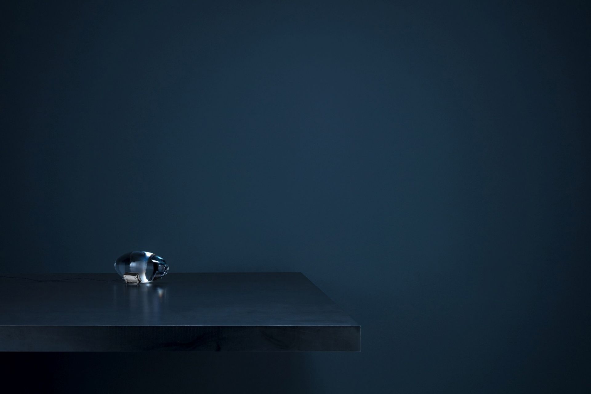 Atman LED Tischleuchte von Catellani & Smith auf dunklem Tisch vor dunkler Wand.