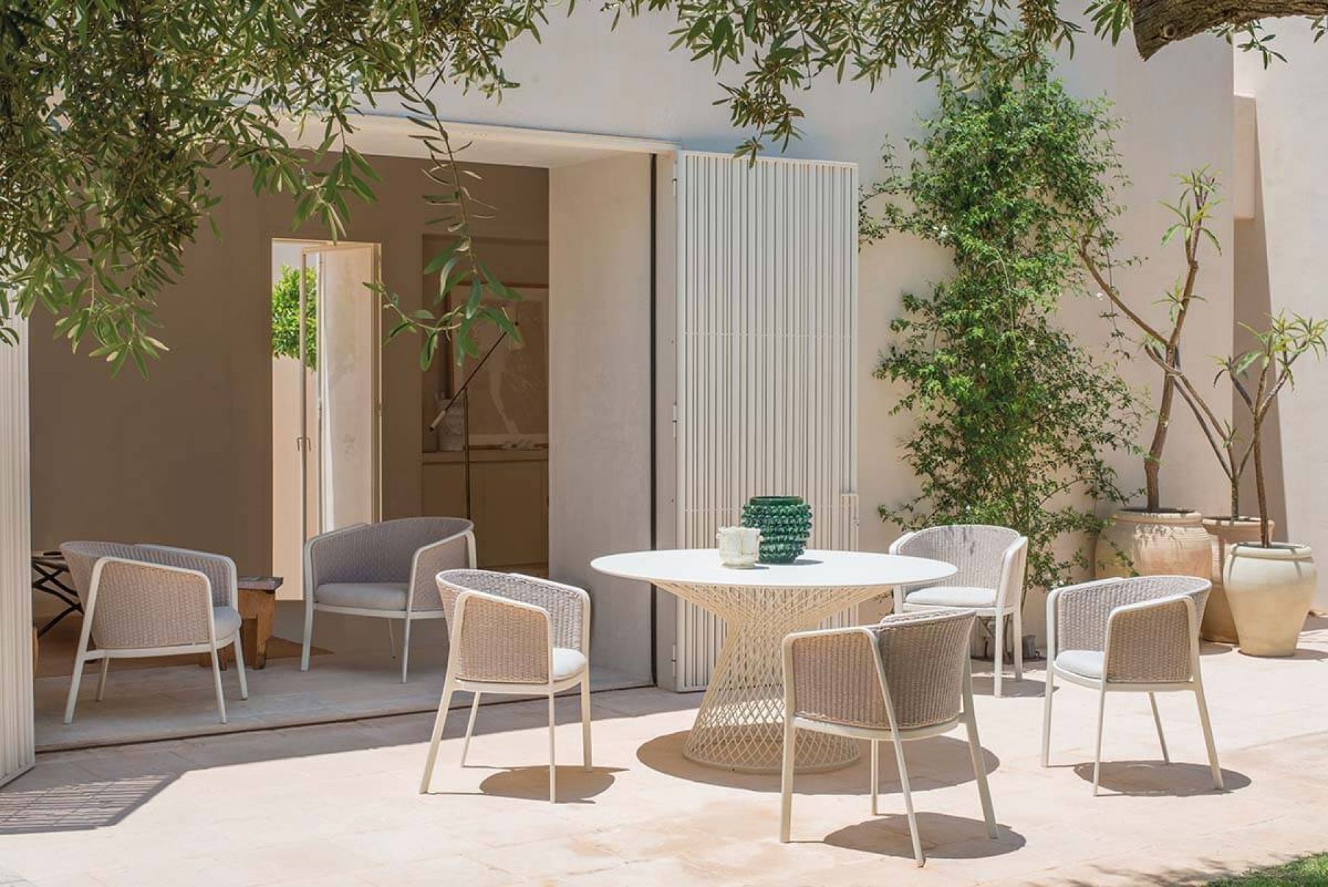 Carousel Armlehnstuhl von Emu, Weiß/Melange Ivory, auf einer Terrasse mit Gartenmöbeln.