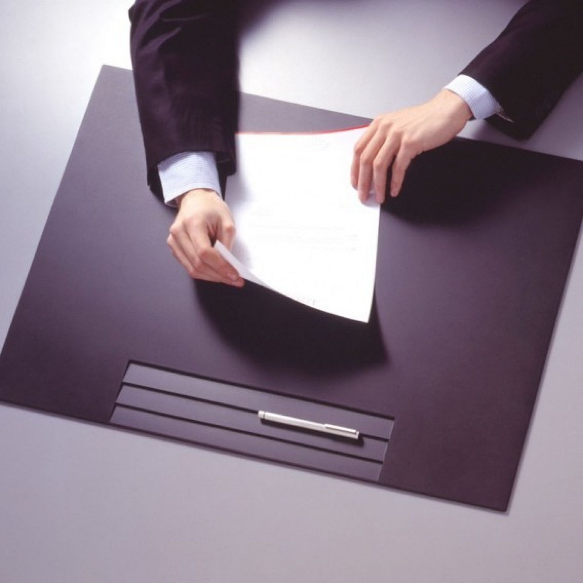 Status Schreibtischunterlage: Hände halten Papier auf der schwarzen Schreibtischunterlage mit Stiftablage. Büroaccessoire für den Schreibtisch.