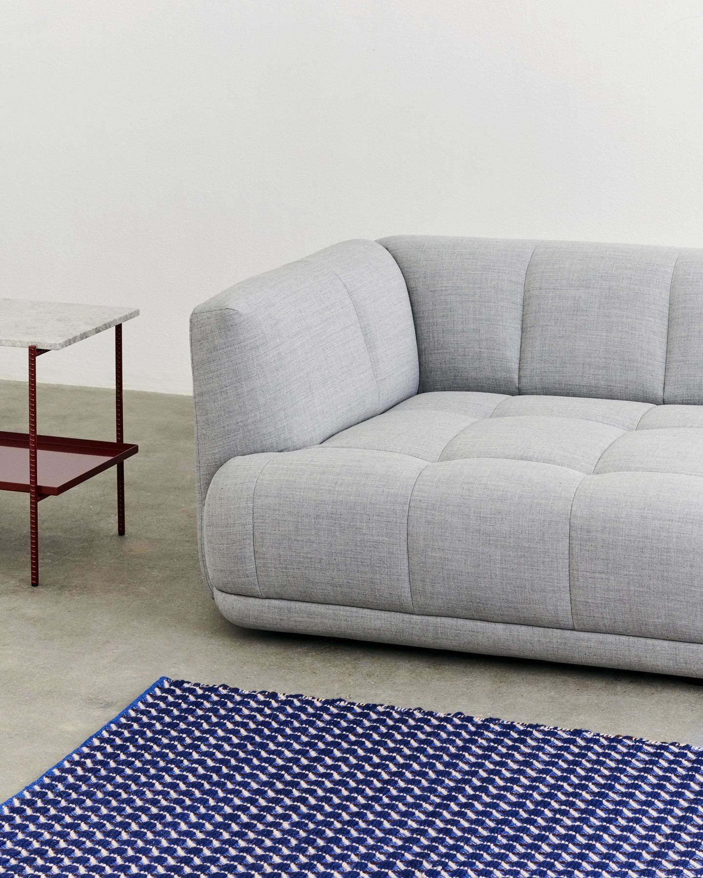 Grauer Rebar Beistelltisch mit Marmorplatte neben einem grauen Sofa und einem blauen Teppich.