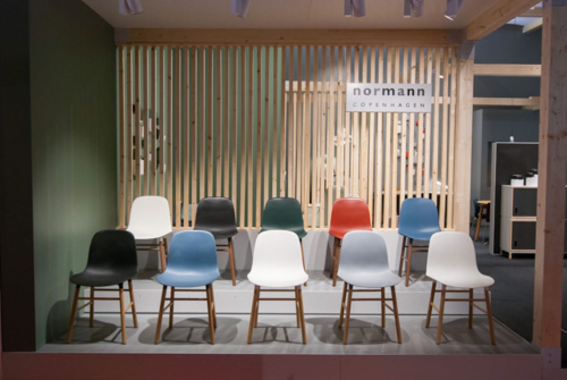 Reihe von bunten Form Chair Stühlen von Normann Copenhagen mit Holzbeinen vor Holzwand.