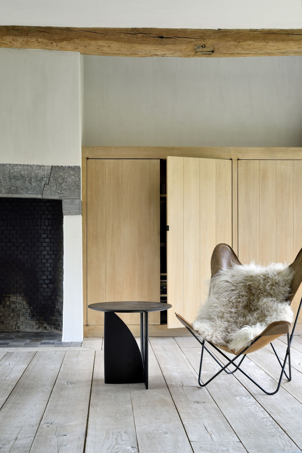 Geometric Beistelltisch Eiche Ethnicraft neben Sessel mit Fell in modernem Wohnzimmer.