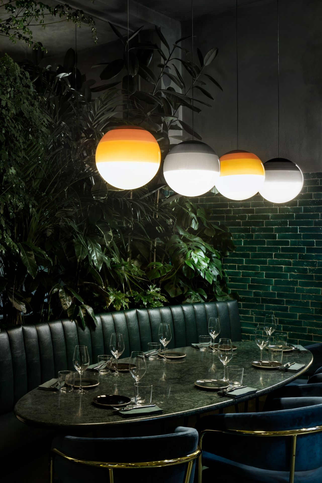 Dipping Light Pendelleuchten in Grün und Orange über einem gedeckten Tisch in einem Restaurant.