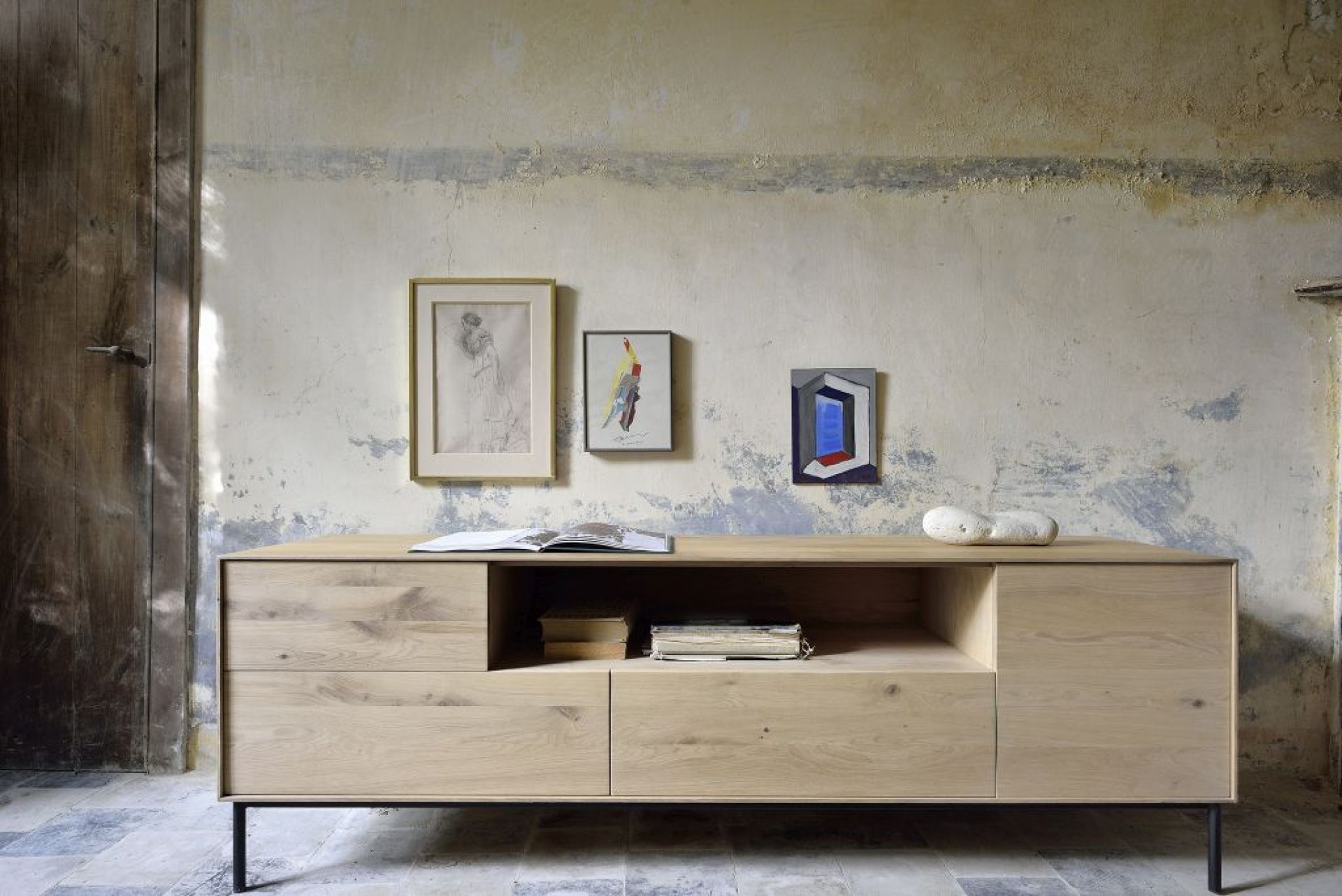 Whitebird TV Möbel von Ethnicraft aus hellem Holz mit Schubladen und Ablageflächen vor rustikaler Wand.