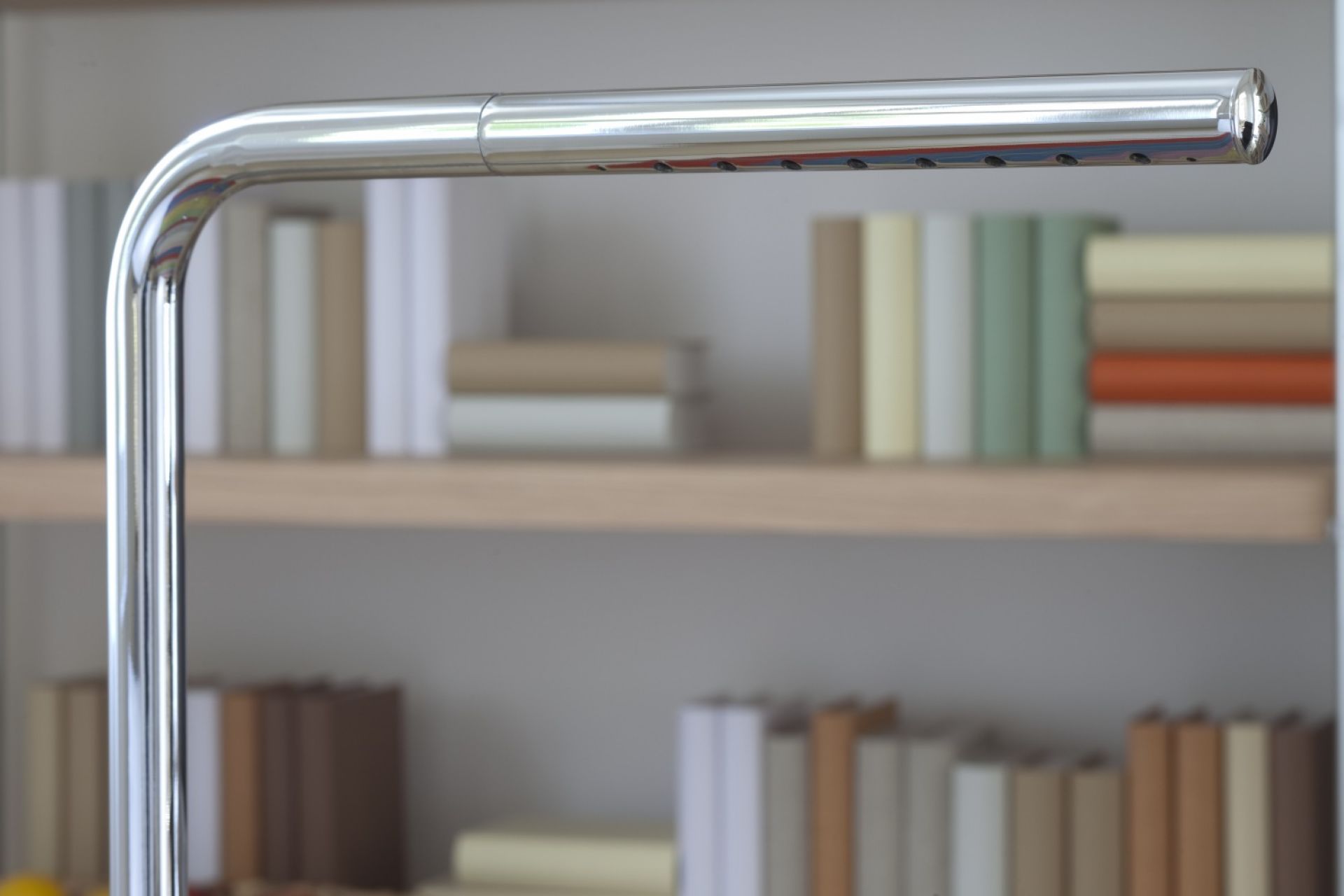 Nahaufnahme der verchromten Lum Tischleuchte von Thonet vor einem Bücherregal.