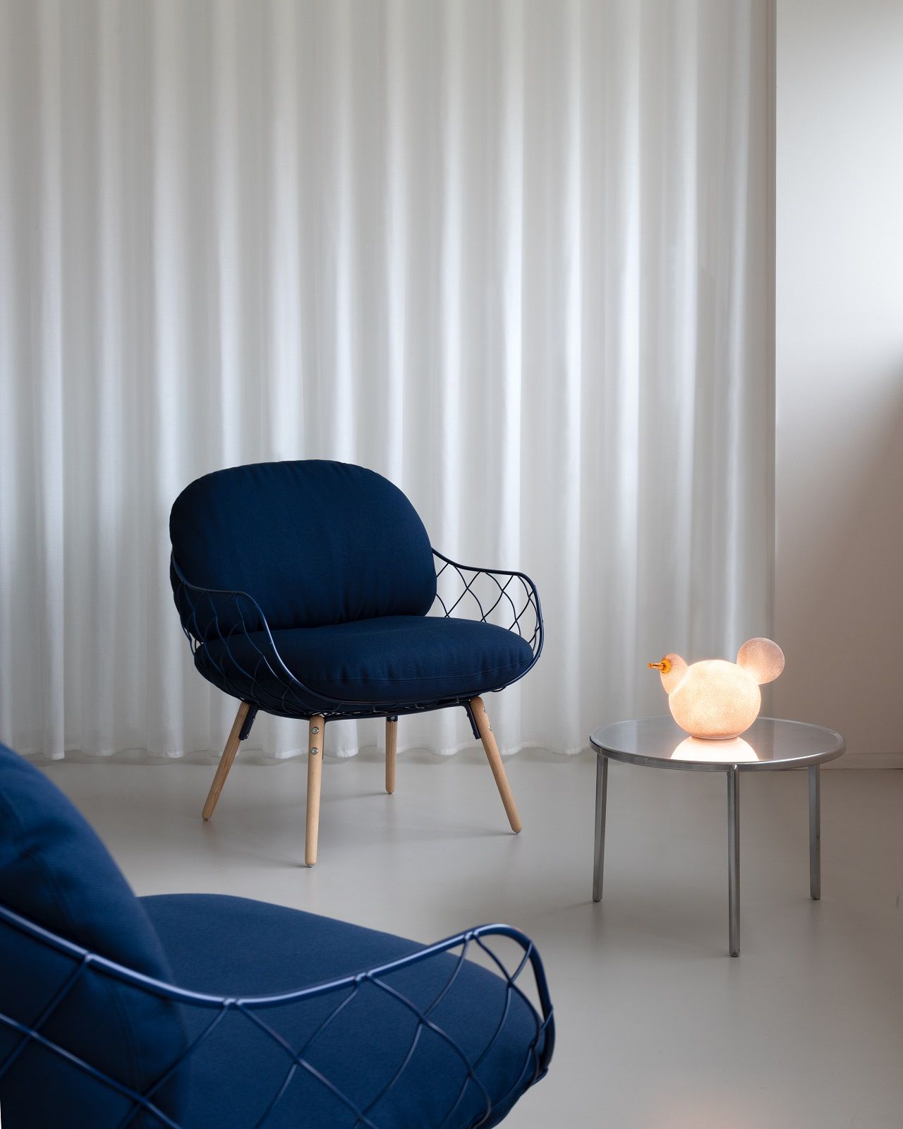 Magis Tambour Beistelltisch: Runder, silberner Couchtisch mit Lampe in modernem Wohnzimmer neben blauen Sesseln.